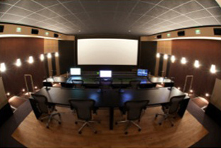 A wide conference room featuring a large projection screen, several computer monitors, and a long dark table.