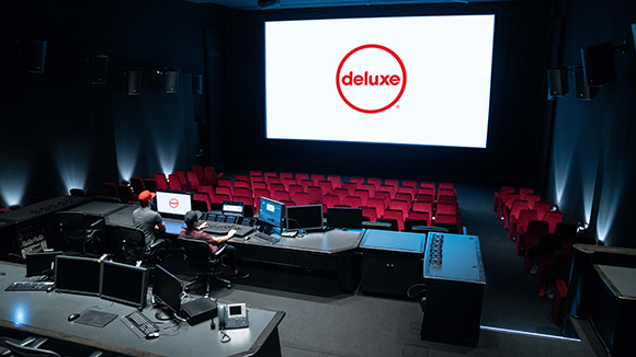 A dark movie theater with rows of red seats and a large screen showing a red Deluxe logo.