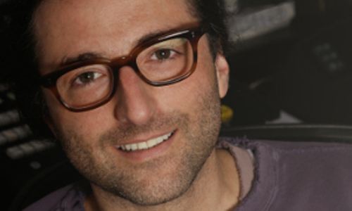 A man with dark hair and brown-rimmed glasses smiling at the camera.