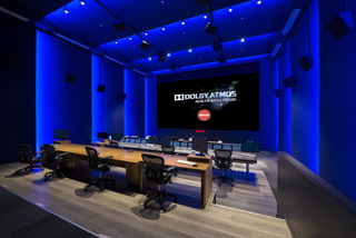 A dark film mixing studio with blue lighting, a large screen displaying Dolby Atmos, and a long mixing console.