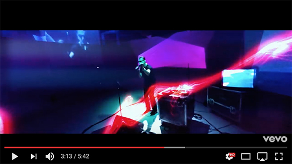 A person sings into a microphone amidst red and purple light projections in a dark space.