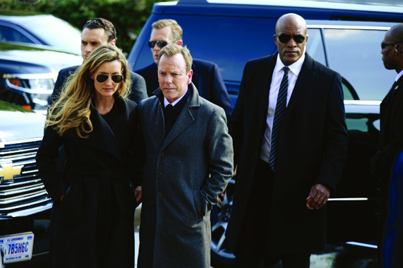 A group of people in dark coats and sunglasses walking together near black SUVs.