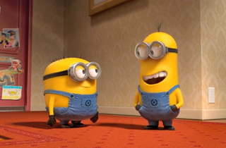 Two yellow Minions in blue overalls standing on a red patterned carpet in a room.