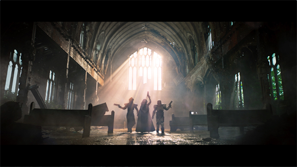 Three silhouetted figures stand in a ruined, sunlit cathedral with broken arches and debris.