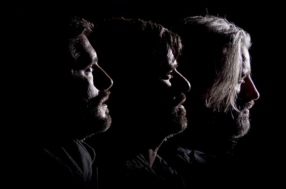 Three men's profiles illuminated by side lighting against a dark background.