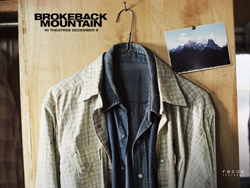Two plaid shirts, one light and one dark, hang on a hook against a wooden wall next to a mountain photograph.