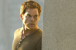 A man with short brown hair wearing a brown shirt looks intensely over a stone wall.
