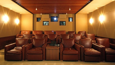 Rows of plush brown leather armchairs arranged in a home cinema with warm lighting.