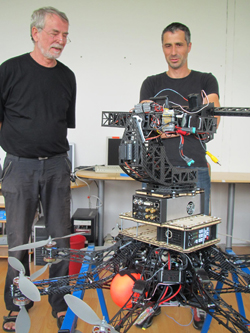 Two men stand beside a large, complex multi-rotor drone prototype in a workshop.