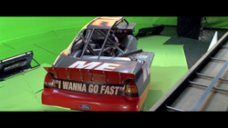 A red and black racing car with the text 'I WANNA GO FAST' sits in a green screen studio.