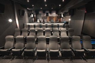 Rows of gray upholstered theater seats in a dark, modern cinema room with ambient lighting.