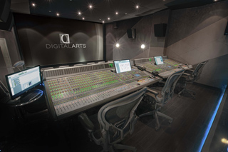 A professional recording studio featuring large mixing consoles, computer monitors, and ergonomic chairs.