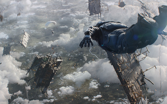 A person in dark tactical gear falls through a cloudy sky surrounded by large pieces of falling debris.