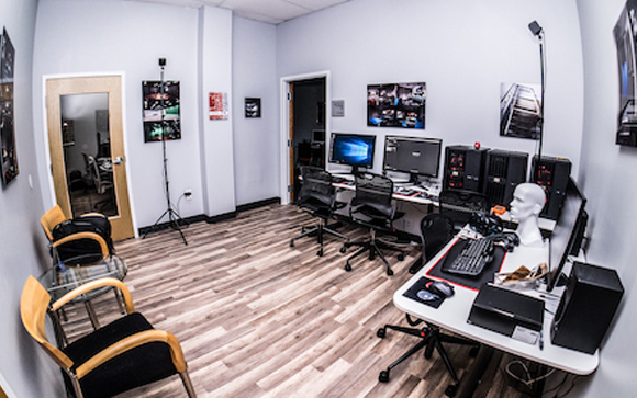 A wide-angle view of a professional office containing several computer workstations and black office chairs.