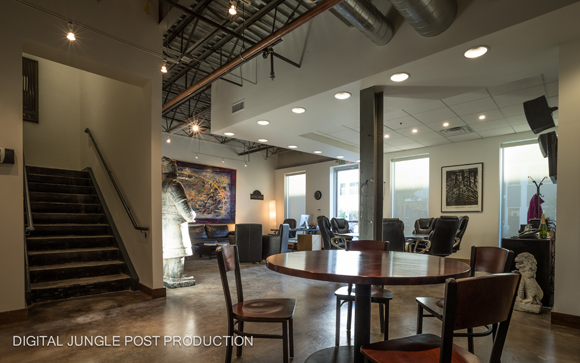 A modern office interior with high ceilings, a staircase, a large statue, and a round wooden table.