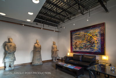 Three large terracotta warrior statues stand against a wall next to a black leather sofa and abstract art.