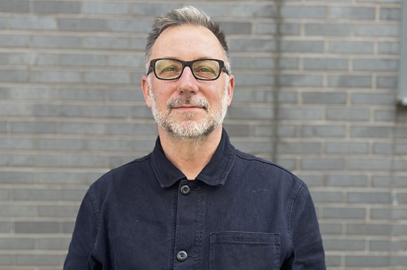A man with graying hair, glasses, and a salt-and-pepper beard wearing a dark button-down shirt.