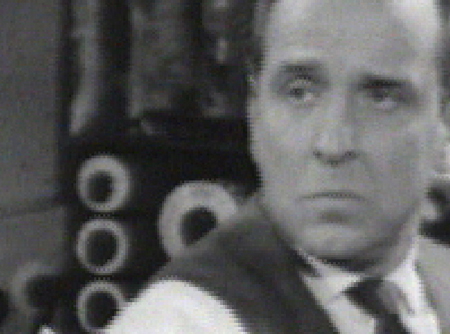 A man in a collared shirt and tie looking to the side with a somber expression.