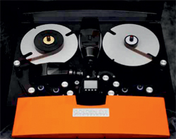 A black reel-to-reel tape recorder with two silver reels and an orange cover in the foreground.