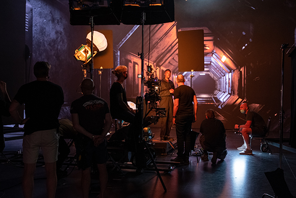 Film crew members working on a set featuring a large digital screen displaying a futuristic corridor.