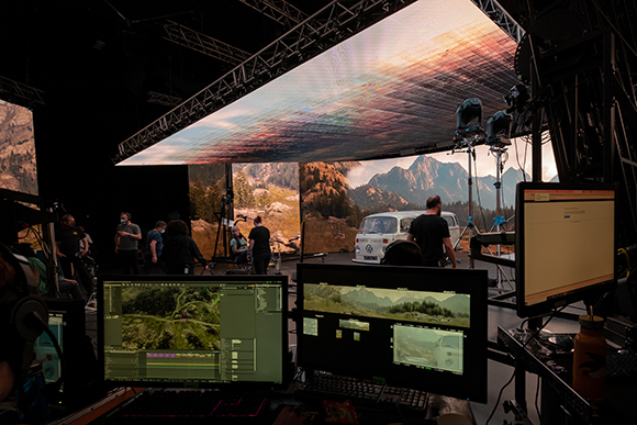 Production crew in a dark studio working with large LED screens displaying mountain landscapes.