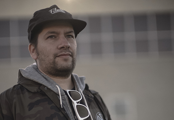 A man in a black cap and camouflage jacket looks into the distance against a blurred background.