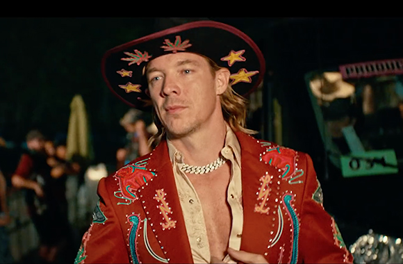A man wearing a wide-brimmed cowboy hat with gold stars and a red embroidered western jacket.