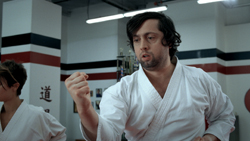 A man in a white gi holds a clenched fist in a martial arts studio.