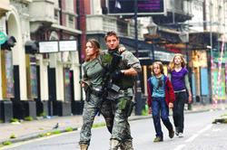 A man in camouflage holding a rifle and a woman in tactical gear walk with two children down a city street.