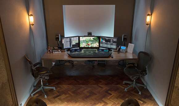 A workstation with three computer monitors, studio speakers, and a large white screen in a dim room.