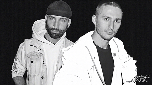 Black and white portrait of two men looking at the camera against a dark background.