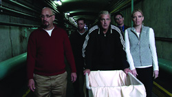 Five people walk through a dark, industrial tunnel toward the camera.