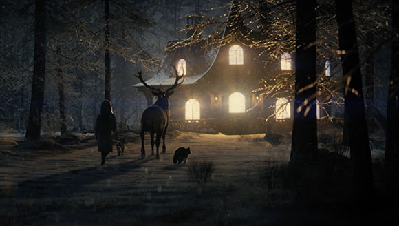 A person and a large deer walk with two dogs toward a brightly lit house in a dark, snowy forest.
