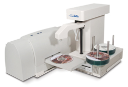 A white laboratory machine with a mechanical arm and several optical discs on spindles.