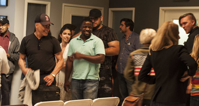 A diverse group of people stand together in an indoor setting, with some individuals smiling and engaged in conversation.