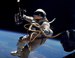 An astronaut in a white spacesuit floats in orbit above the blue curve of Earth against the blackness of space.