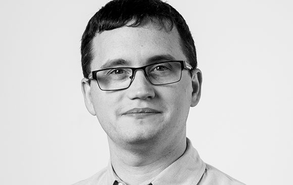 Black and white headshot of a man with short dark hair and glasses looking forward.