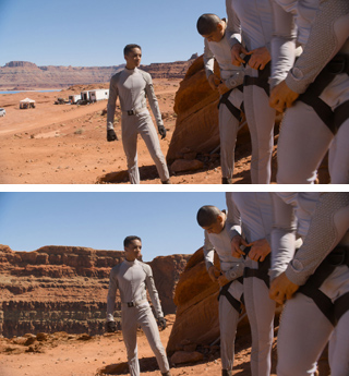 A person in a grey jumpsuit stands in a red desert landscape next to others in similar attire.