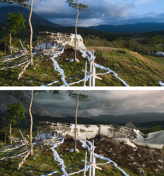 A damaged white structure sits on a grassy hill against a backdrop of mountains and a cloudy sky.