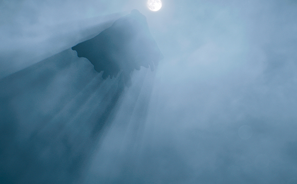 Sunlight beams piercing through dense, blue-toned fog and clouds.