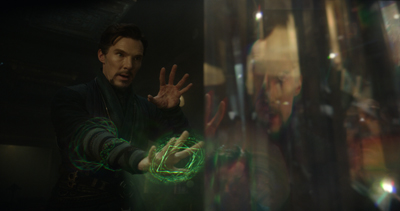 A man in dark clothing extends his hands, one glowing with a green magical energy circle.