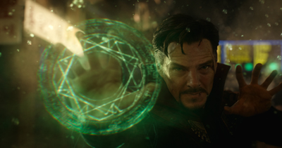 A man with dark hair and a goatee holds up his hands as a glowing green circular magical sigil appears.