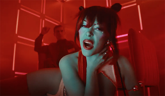 A woman with dark hair and buns leans forward in a room bathed in red light.