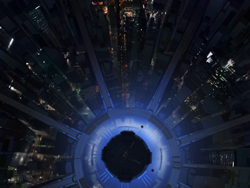 Looking down from a high skyscraper at night into a dark city street with glowing building lights.