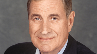 A middle-aged man with short brown hair smiling against a gray background.