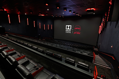 Empty movie theater with black leather reclining seats and a large screen displaying Dolby Cinema and AMC Prime logos.