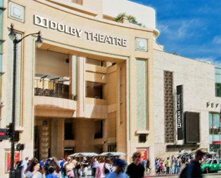 The facade of the Dolby Theatre in Los Angeles under a blue sky with people walking in front.