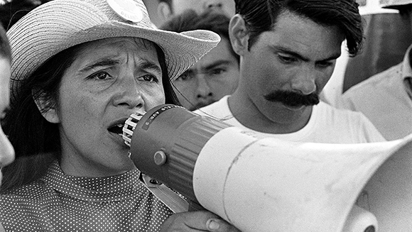 A woman in a wide-brimmed hat speaks into a megaphone during a gathering.