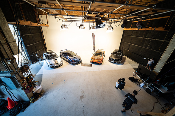 Four colorful modified cars parked in a large white studio with professional lighting and crew members.