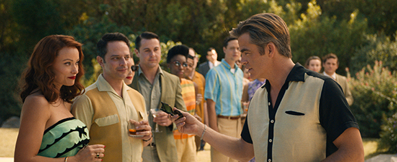 A group of people in mid-century style clothing talking together in a sunny garden setting.
